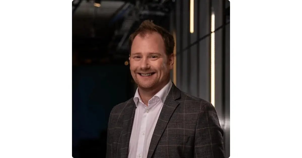 Headshot of a man in a blazer and white shirt in an office setting
