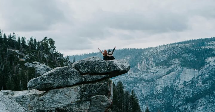 Two people sitting on a rock overlooking a mountain view.