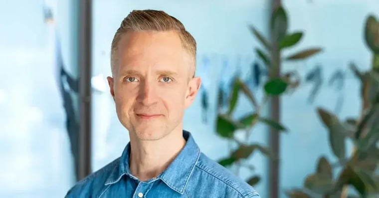 Headshot of a man in a hallway with windows and plants