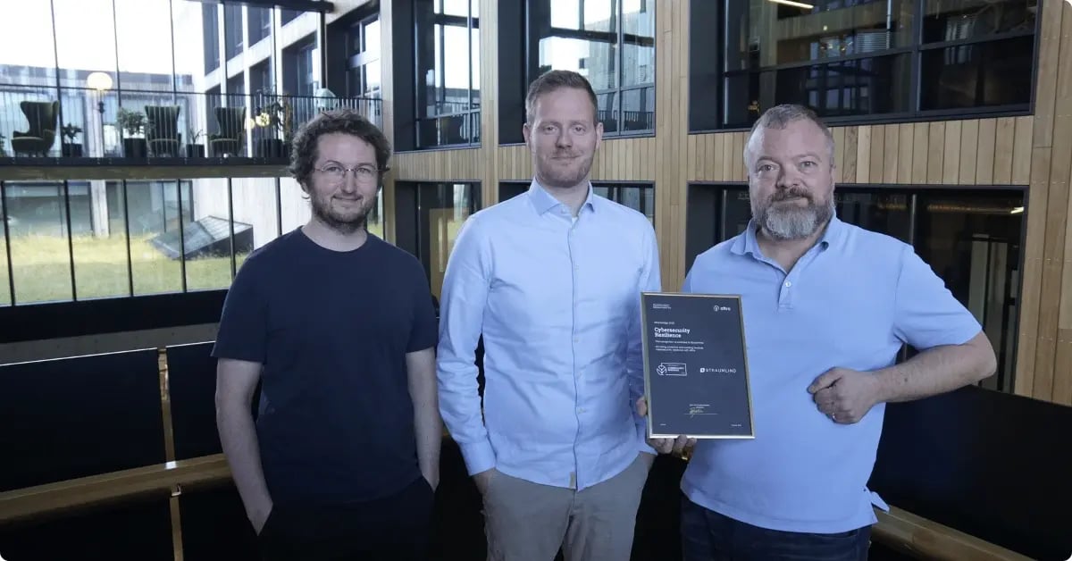 Photo of 3 men standing in a hallway holding a certificate