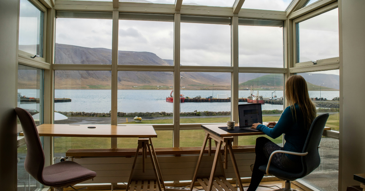 Photo of a woman working in front of a window overlooking the sea and mountains in Reykjavik