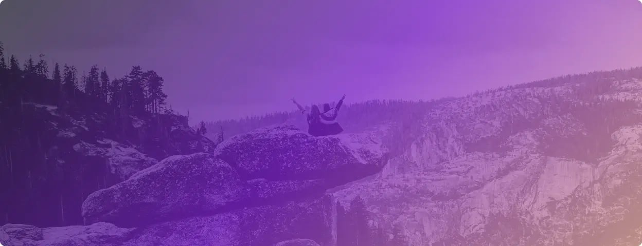 Photo of two people sitting on a rock on a mountain taken from behind