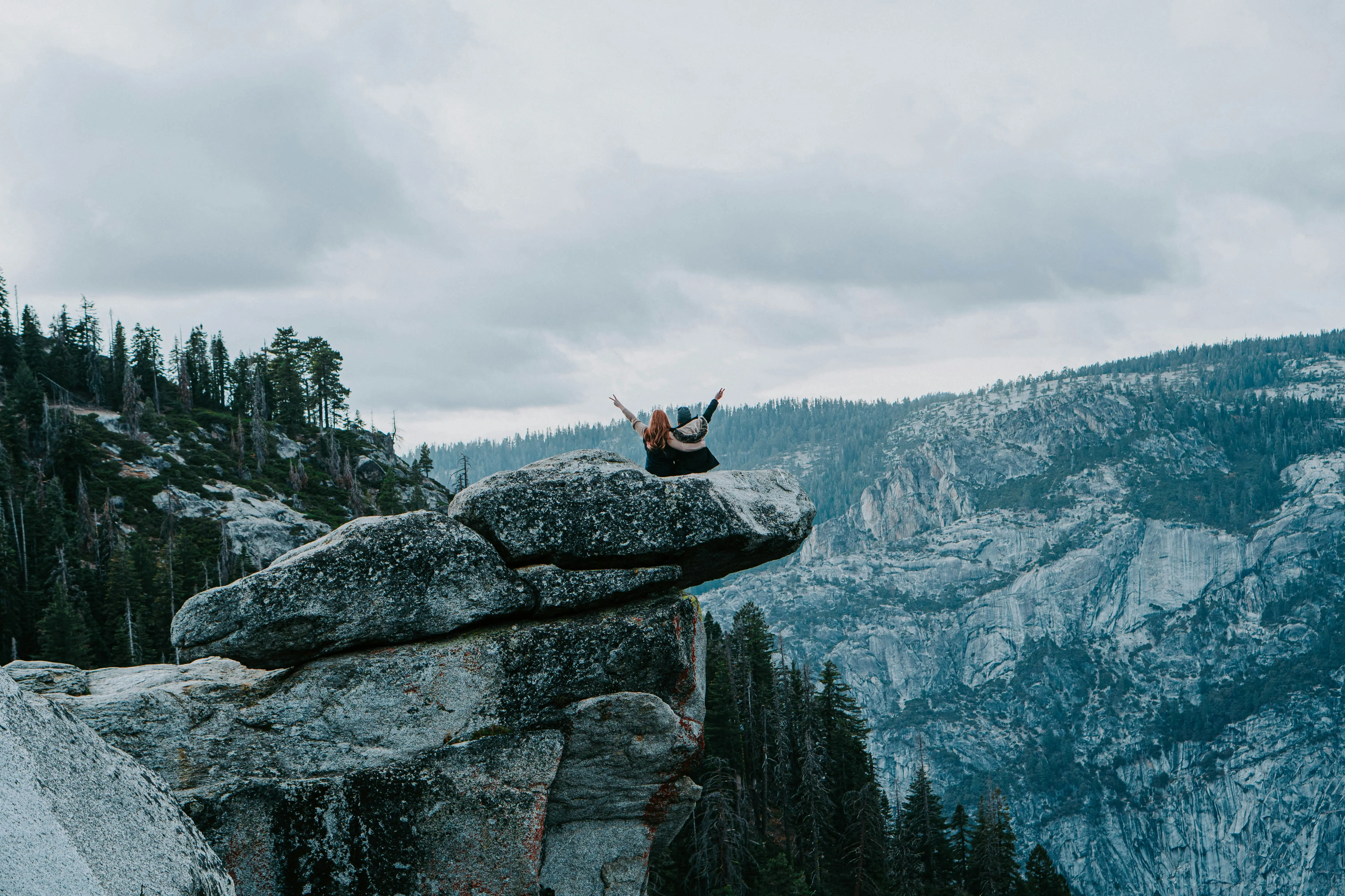 two people sitting on a rock with their back turned to the camera overlooking a mountain view