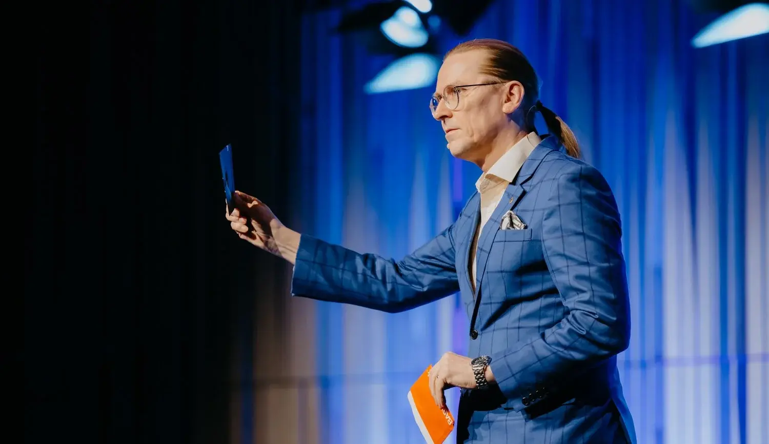middle aged man with glasses and long hair on stage holding a floppy dist