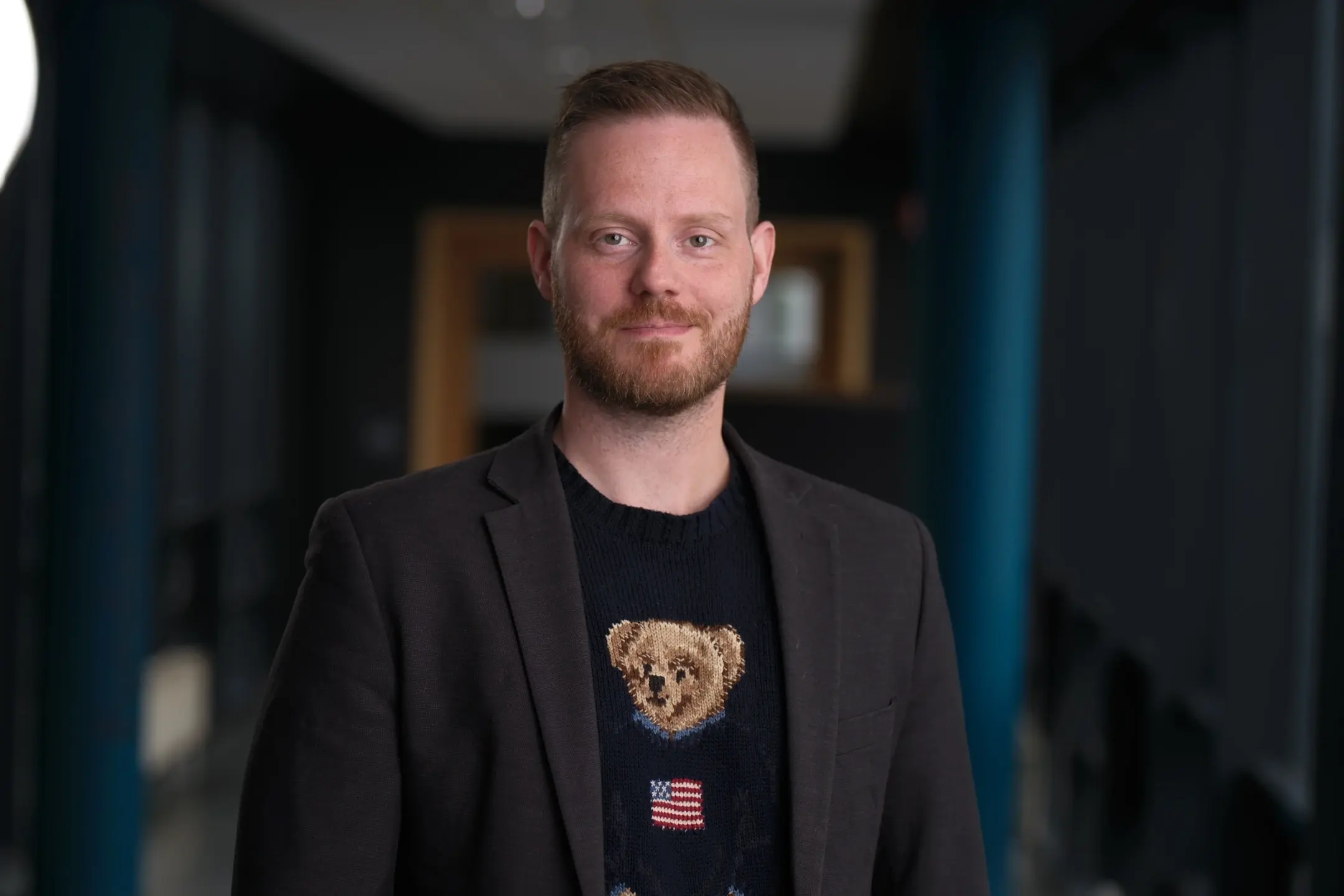 Image of a man in a blazer and a teddy bear t-shirt in an office hallway