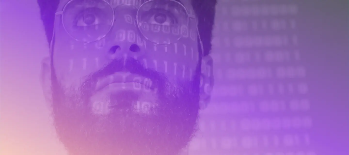 Up close photo of a man with glasses with code reflecting on his face